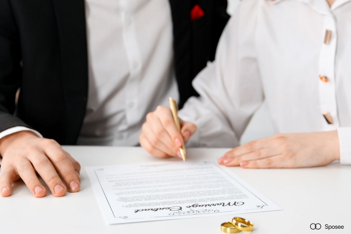 Sposi che firmano contratto con fornitore matrimonio, penna su documento legale